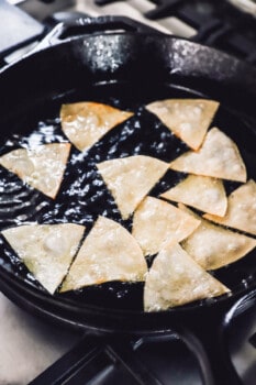 tortilla wedges being fried in a cast iron pan.
