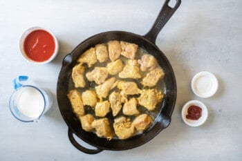 overhead view of chicken cooking in a cast iron skillet.