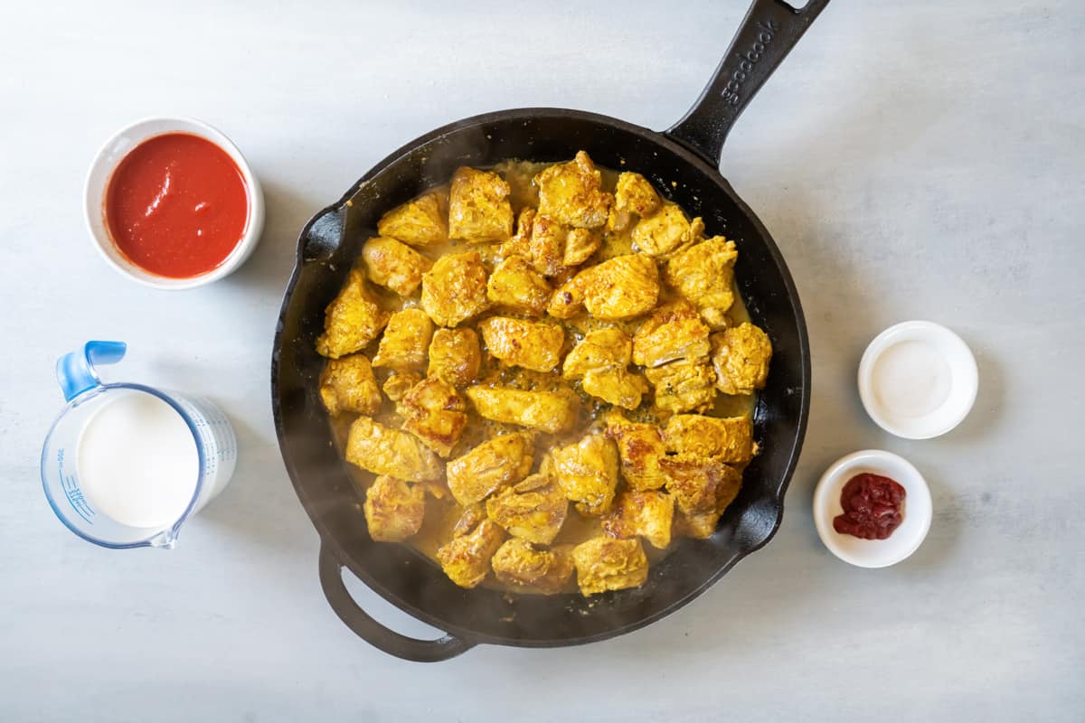 overhead view of chicken cooking in a cast iron skillet.
