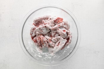 beef strips coated in cornstarch in a glass bowl.