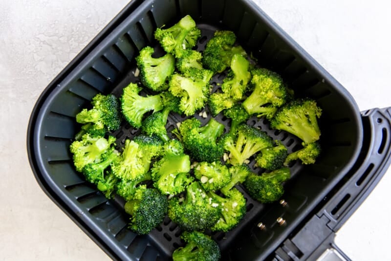 seasoned broccoli in the basket of an air fryer.