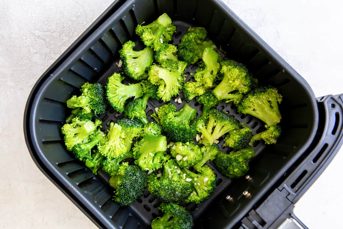 Seasoned broccoli in the basket of an air fryer.