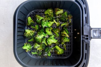 cooked broccoli in an air fryer basket.