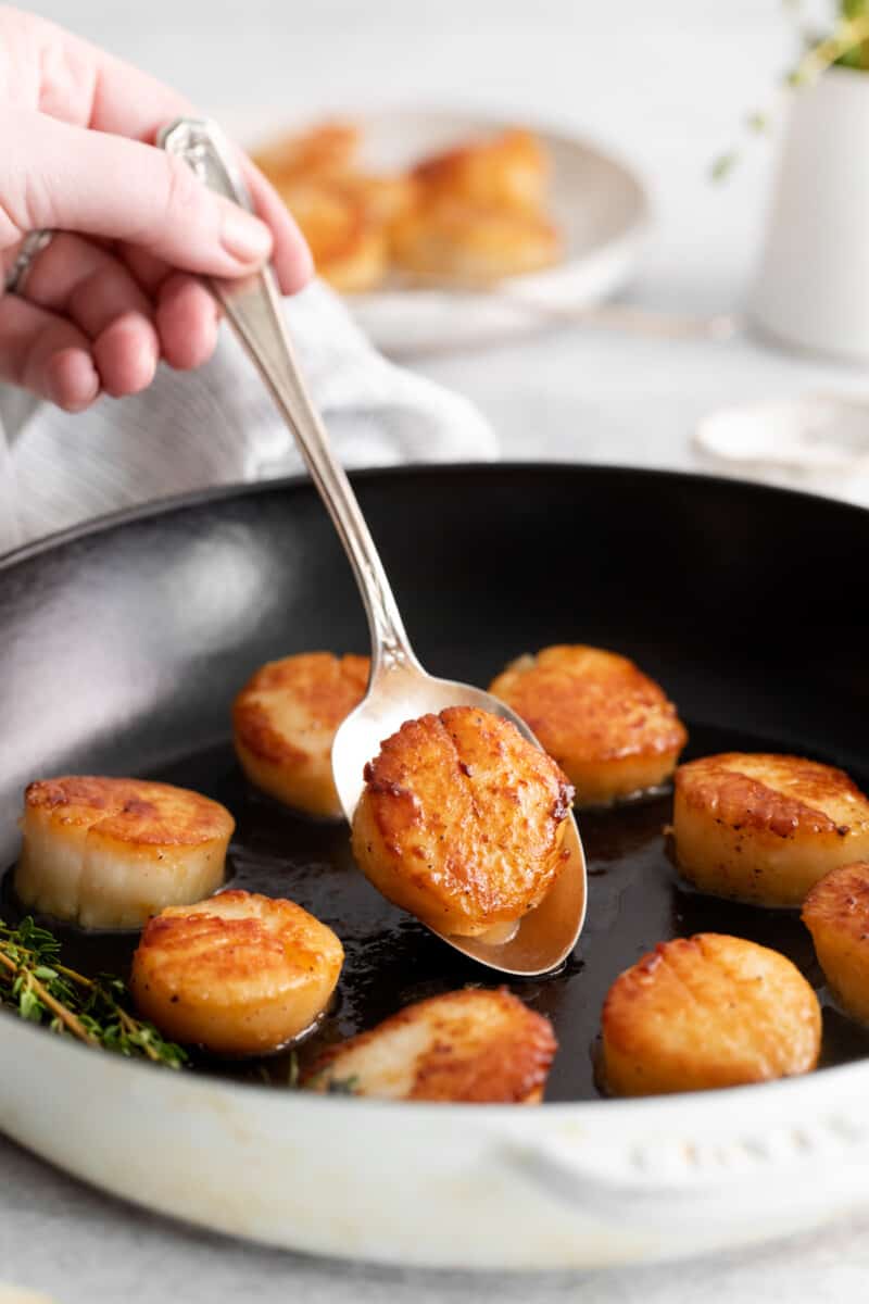 hand picking up a scallop out of a skillet