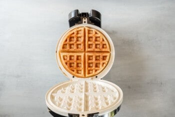 an open belgian waffle iron with a cooked belgian waffle inside.
