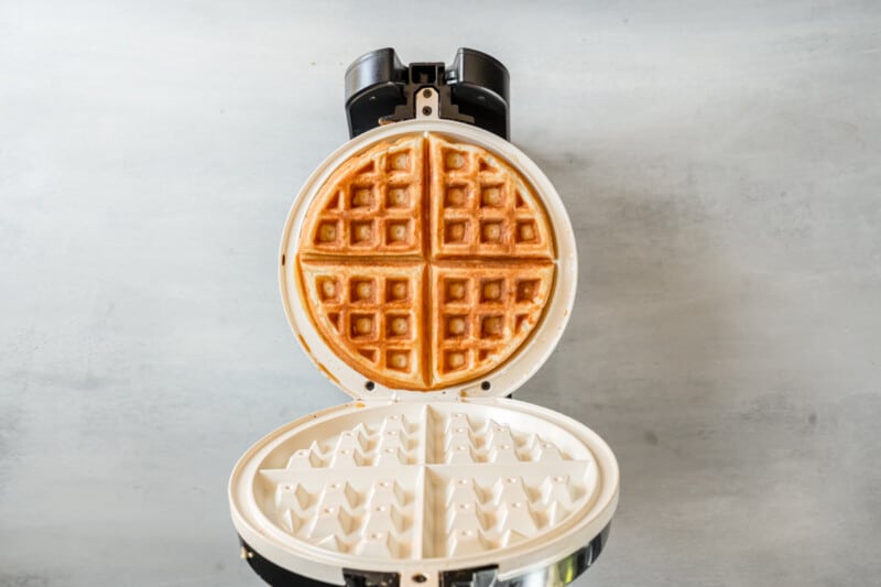 an open belgian waffle iron with a cooked belgian waffle inside.