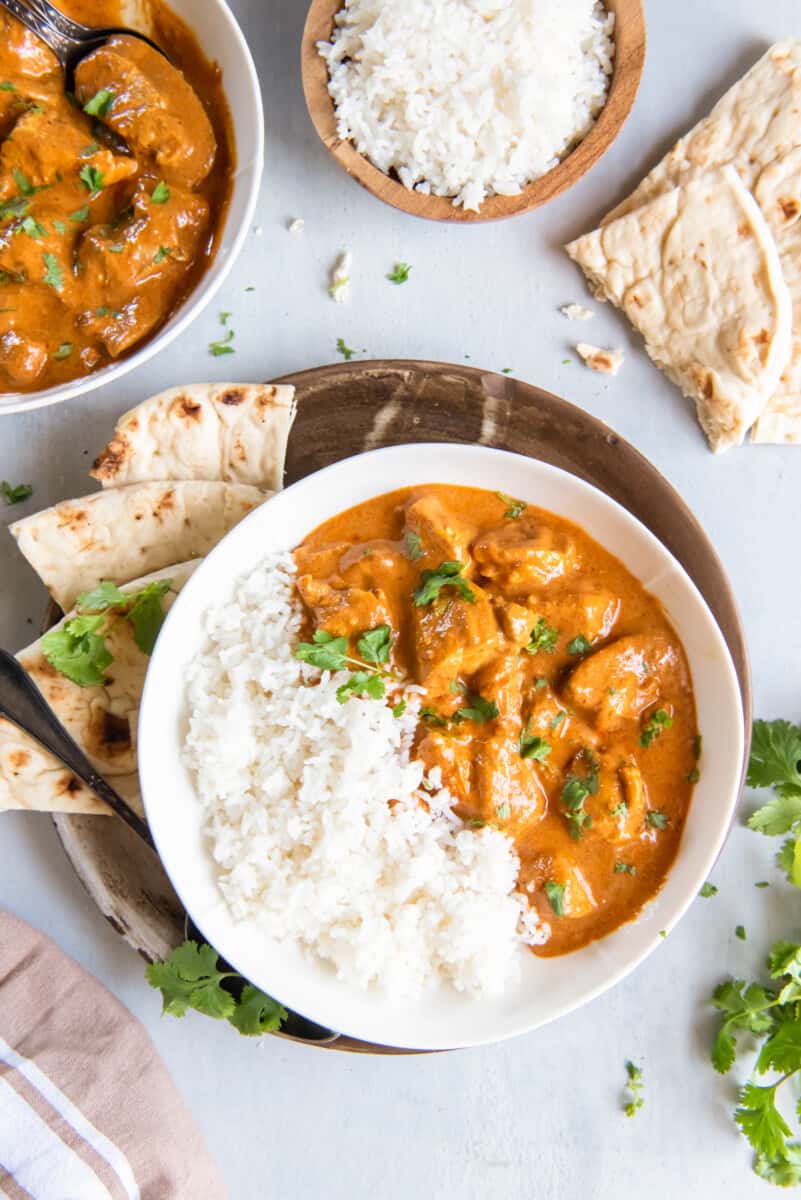 overhead view of indian butter chicken in a white bowl with rice and naan bread.