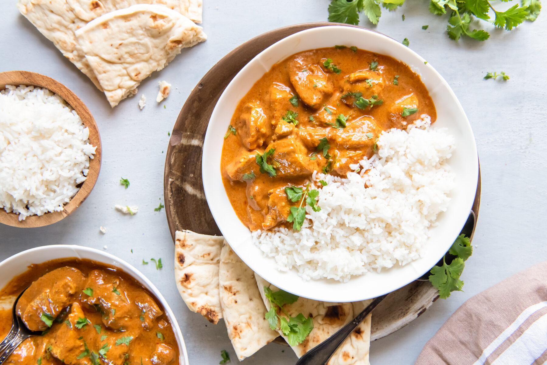 overhead view of indian butter chicken in a white bowl with rice and naan bread.
