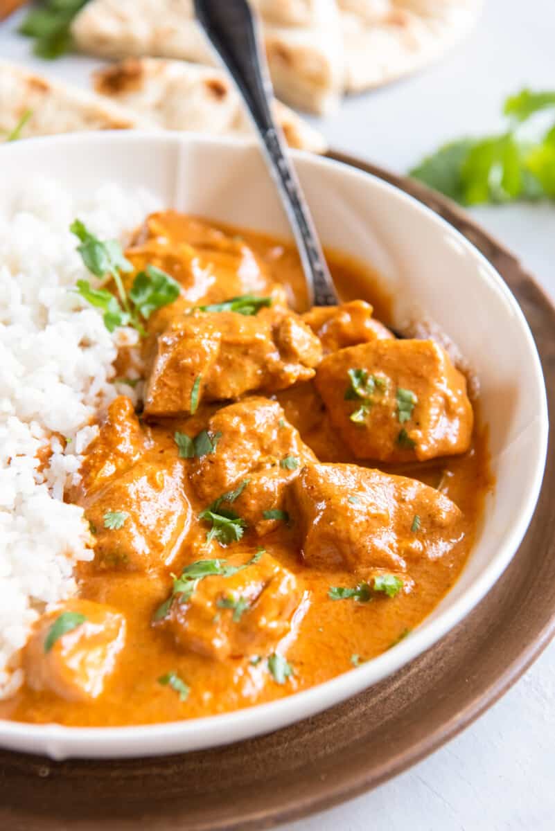 indian butter chicken in a white bowl with rice and a fork.