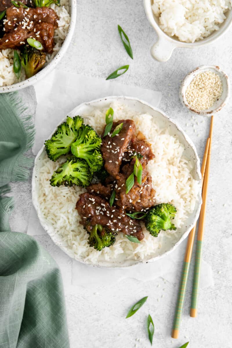 overhead view of instant pot mongolian beef over rice on a white plate with chopsticks.