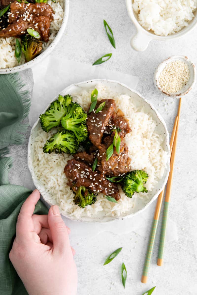 overhead view of a hand grabbing a plate of instant pot mongolian beef with rice.