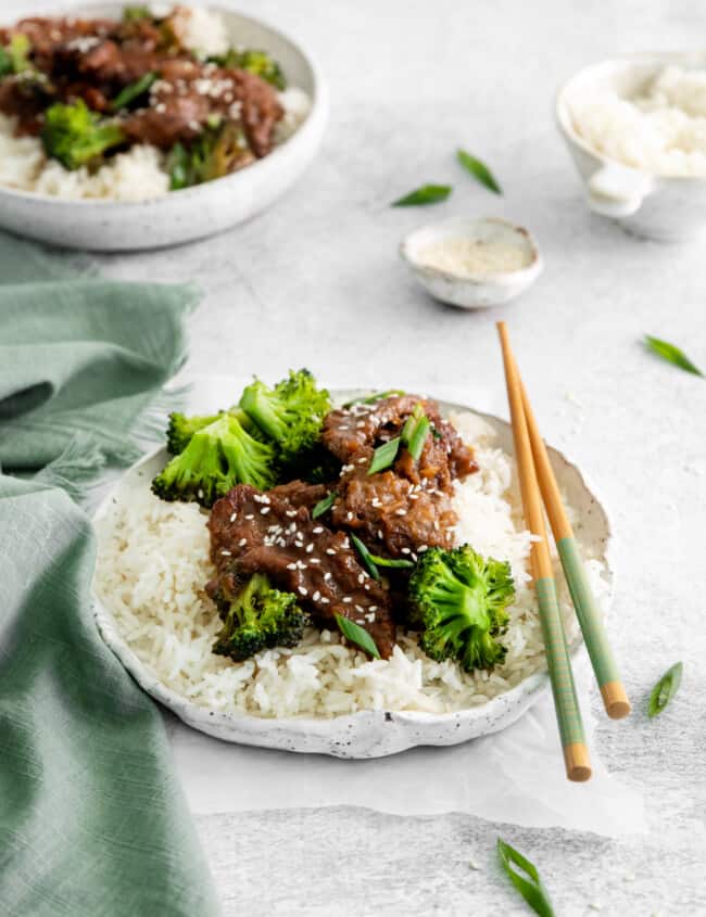 instant pot mongolian beef over rice on a white plate with chopsticks.