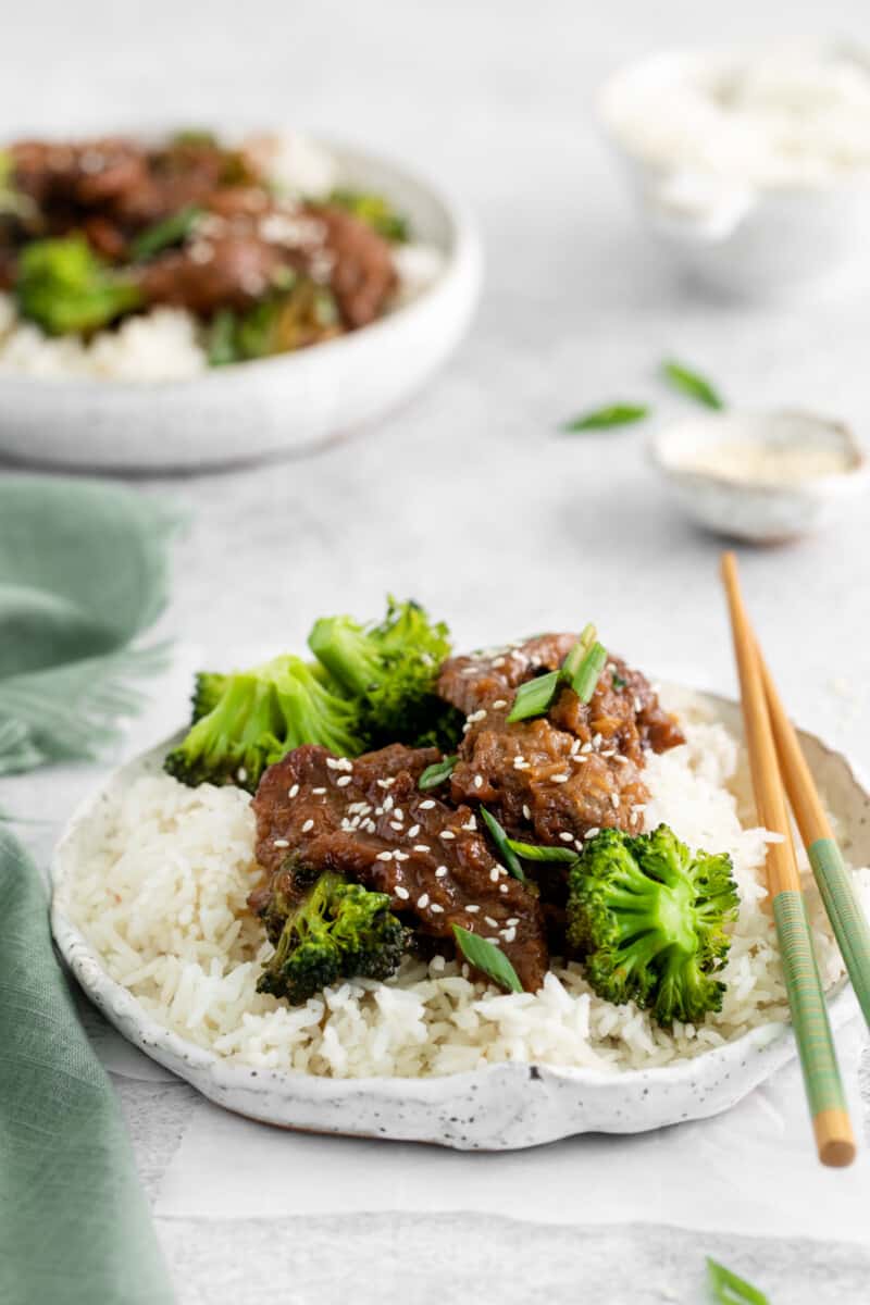 instant pot mongolian beef over rice on a white plate with chopsticks.