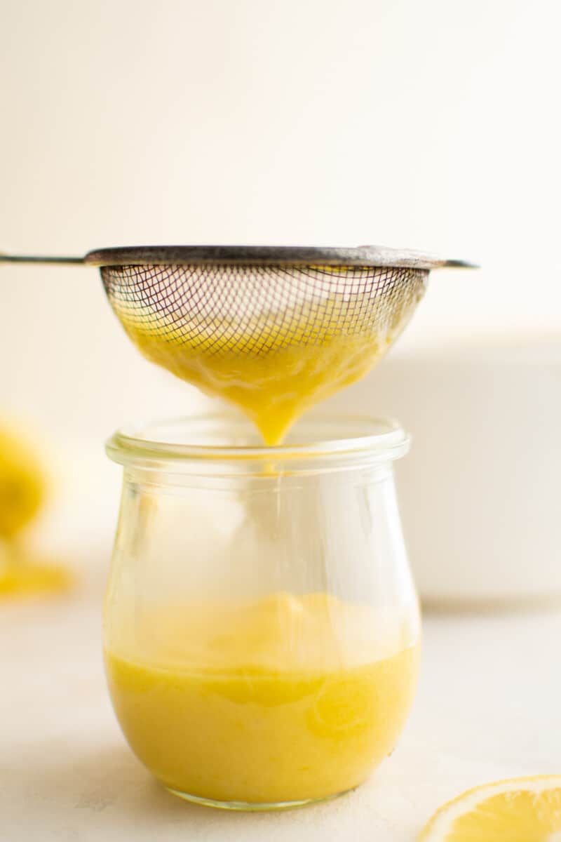 pouring lemon curd through a small sieve, into a jar