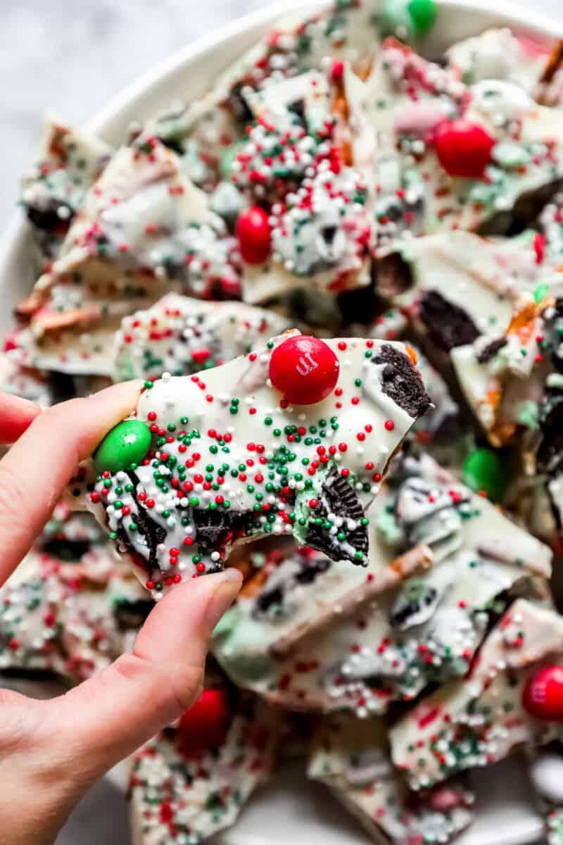 hand holding up a piece of Christmas bark, with M&Ms, sprinkles, and pieces of Oreos
