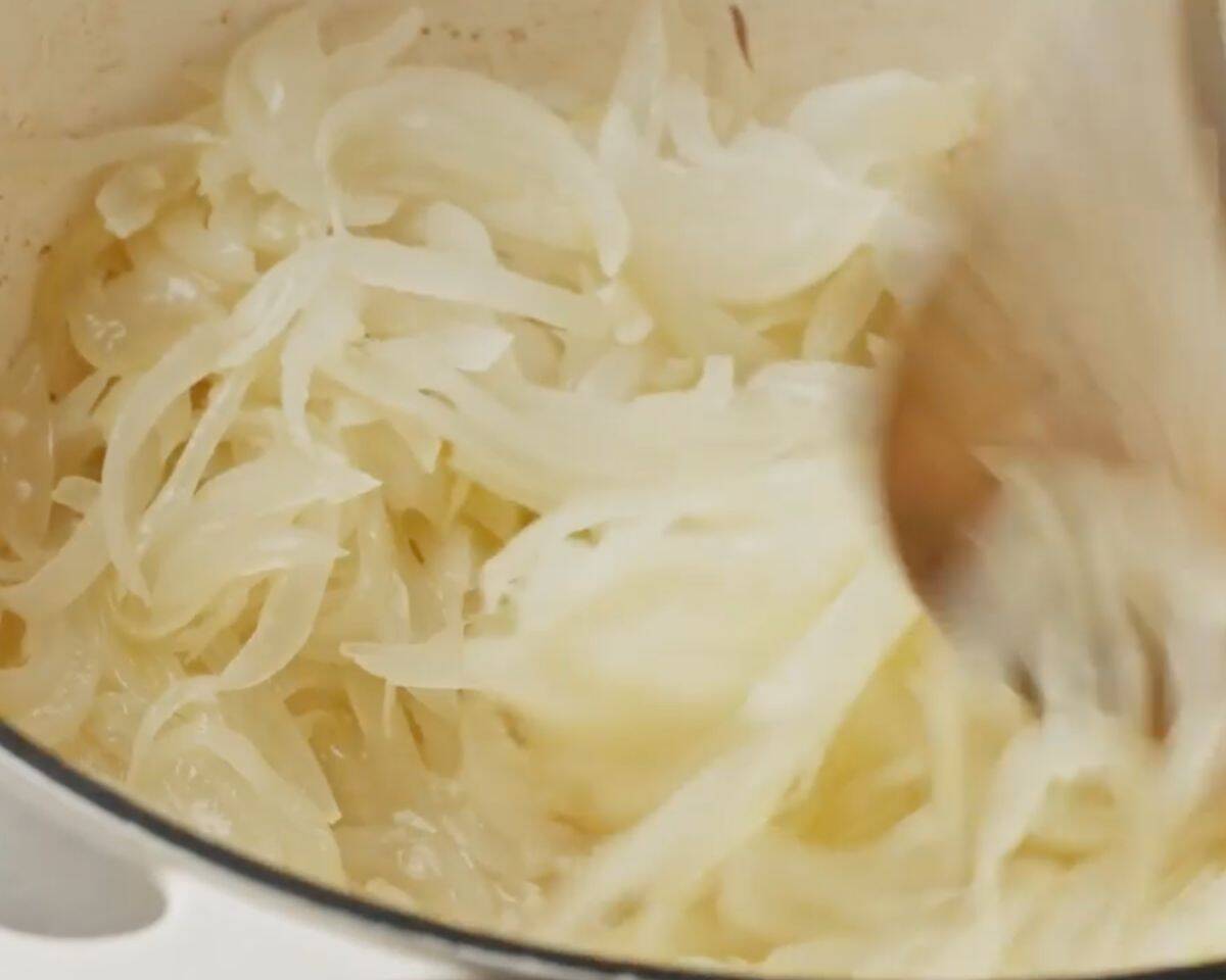 Onions softening and turning translucent while being stirred in a Dutch oven