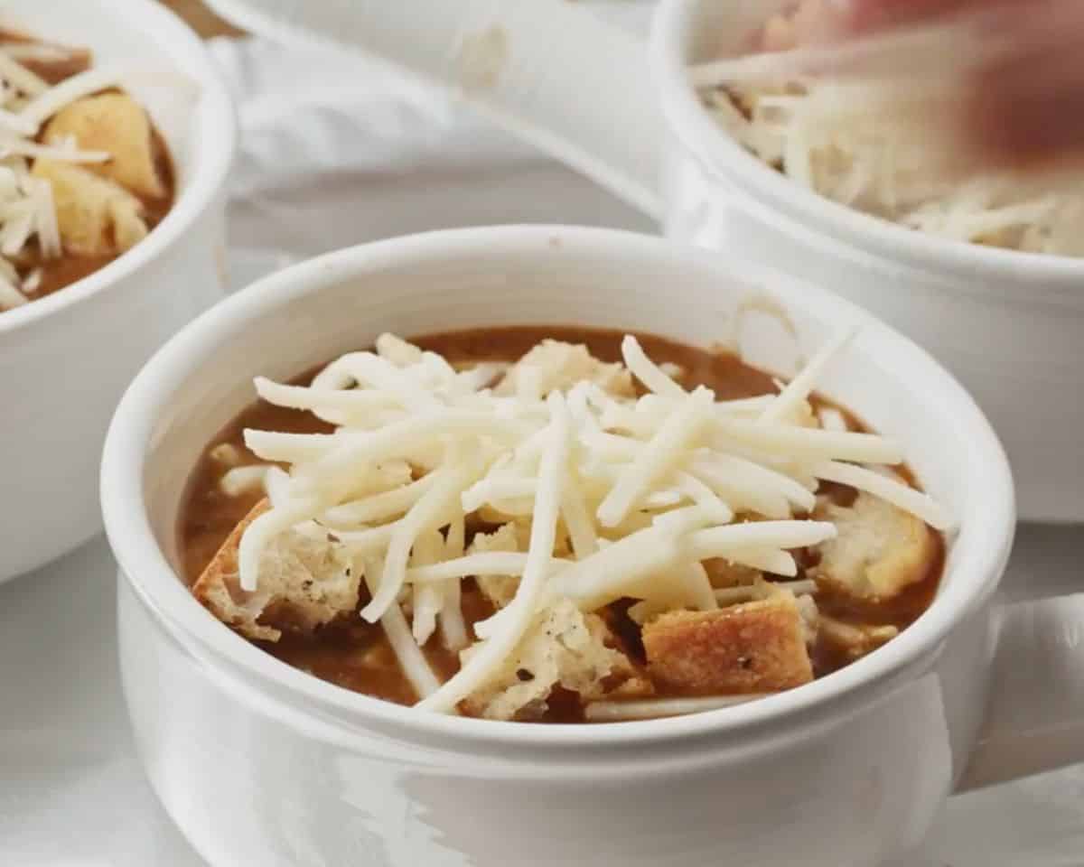 French onion soup in ramekins topped with croutons and shredded Gruyère cheese