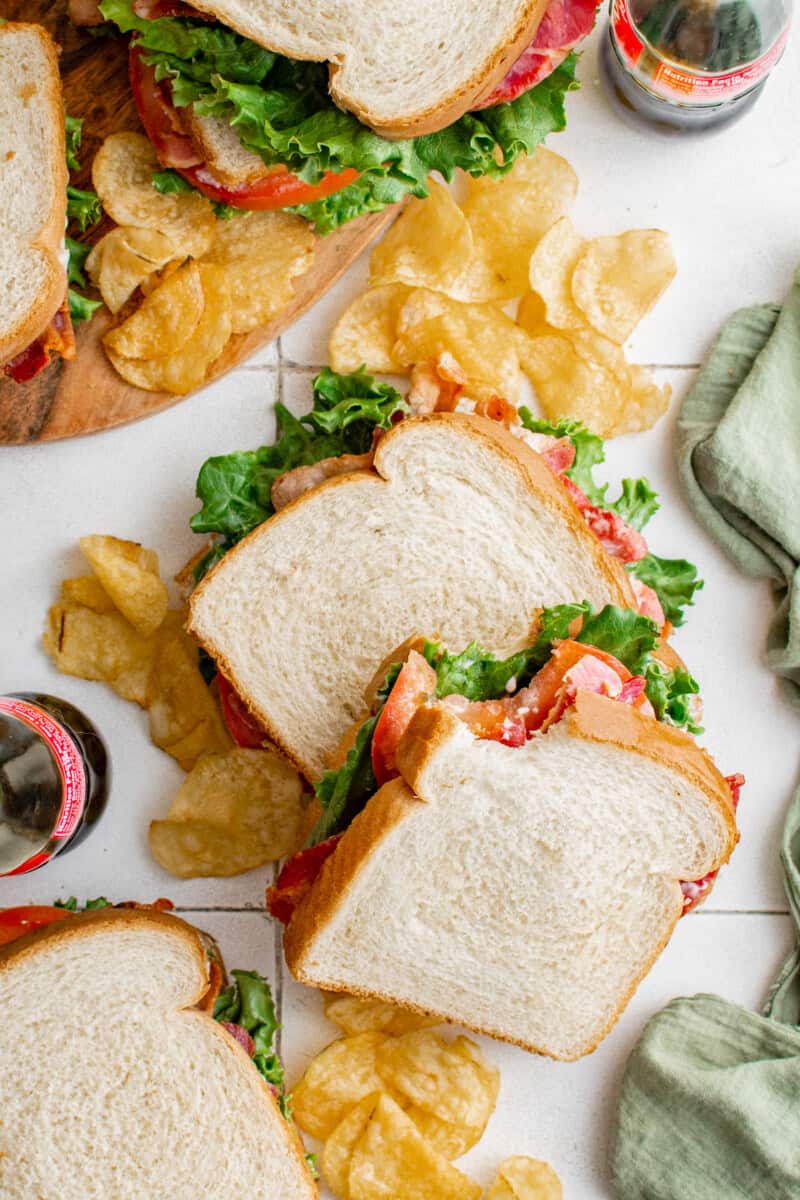 overhead view of a bitten blt sandwich resting atop a second blt sandwich on a bed of potato chips.