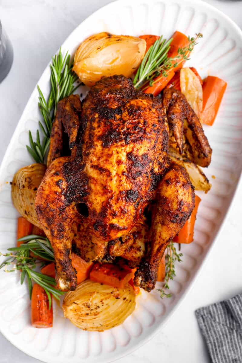 crockpot whole chicken on a white serving platter with vegetables and herbs.