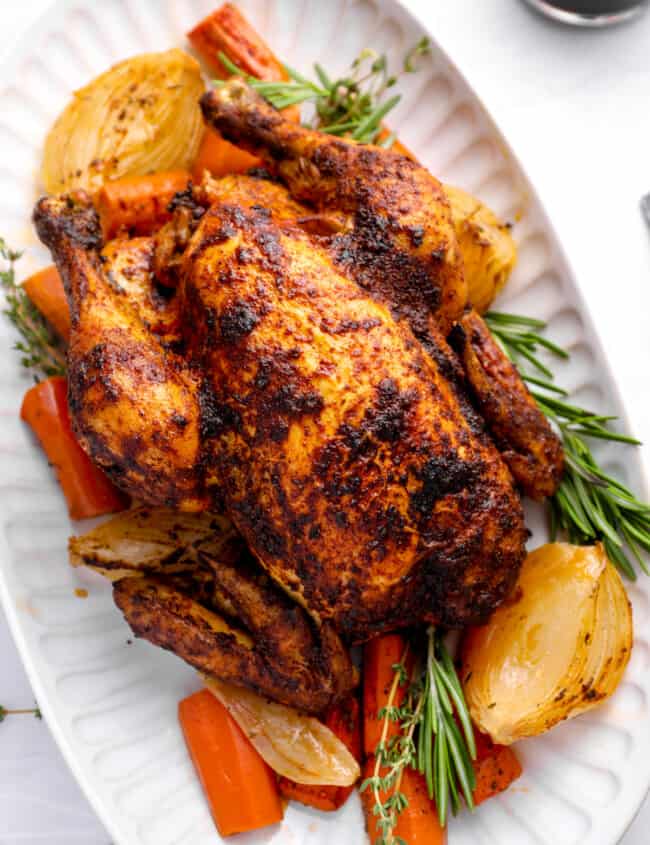 crockpot whole chicken on a white serving platter with vegetables and herbs.