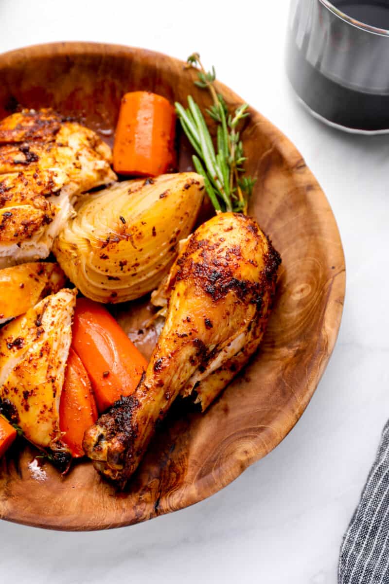 sliced crockpot whole chicken in a wooden bowl with vegetables and herbs.