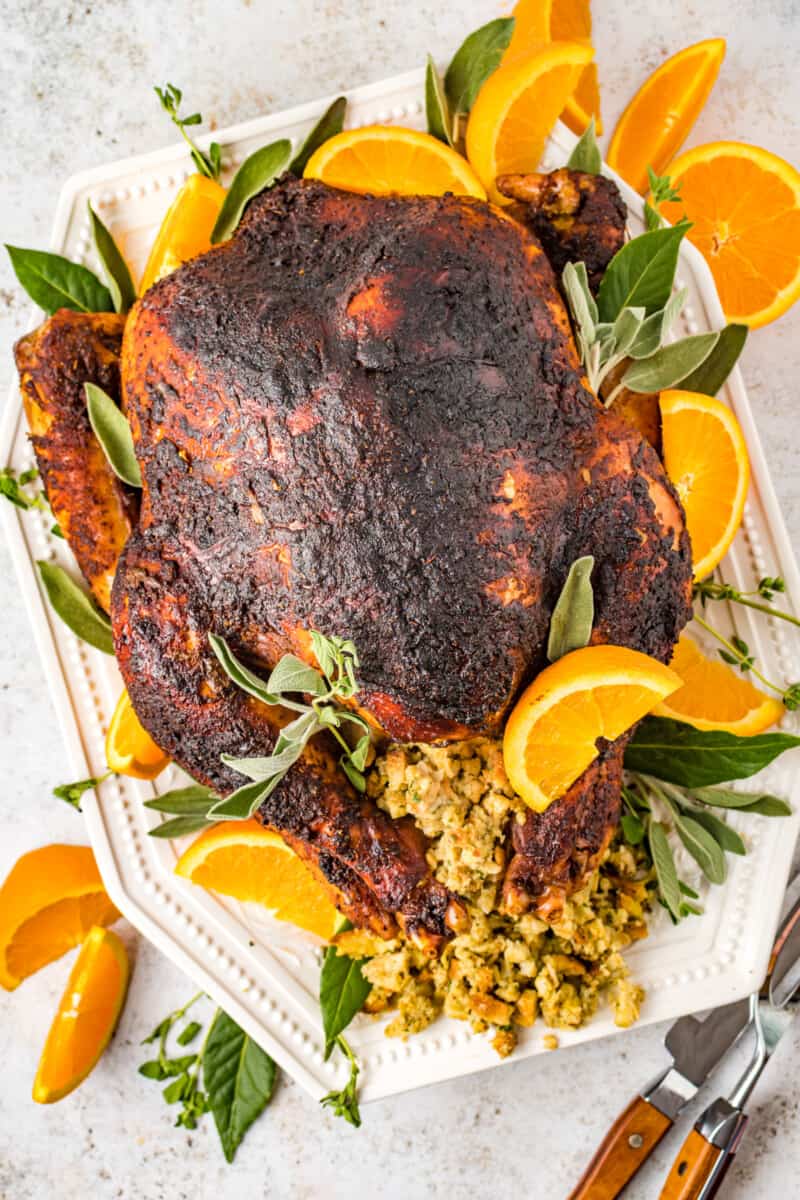 overhead view of dry brined turkey n a white serving dish with sliced oranges stuffing and herbs.