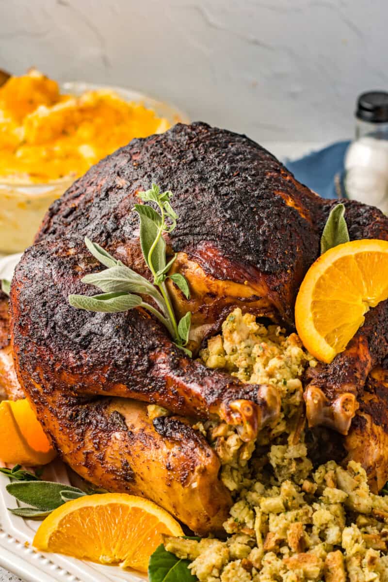 close up of a rubbed whole turkey with stuffing, sage, and orange slices.