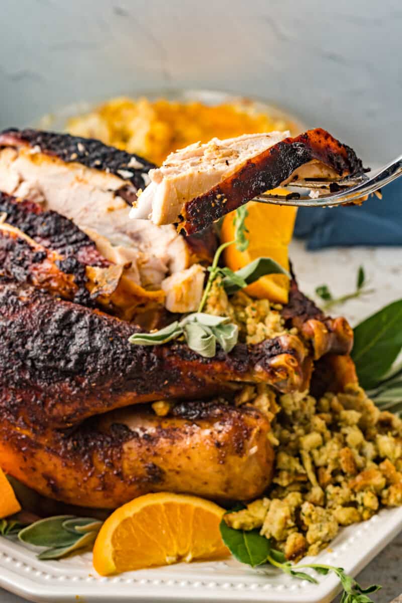 a slice of herb brined turkey held by a fork in front of an herb brined turkey.