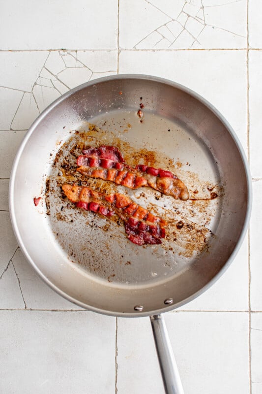 2 strips of cooked bacon in a frying pan.