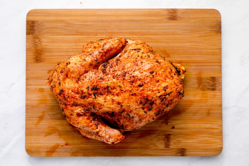 a whole chicken rubbed with herbs on a cutting board.