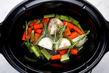 chopped vegetables and herbs in the bottom of a crockpot.
