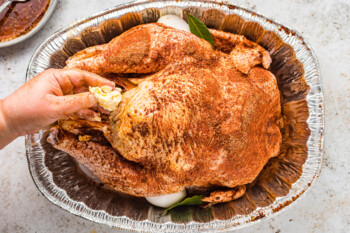overhead view of a hand buttering a raw herb brined turkey in an aluminum roasting pan.
