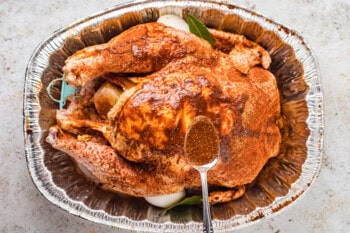 overhead view of juices spooned over a dry brined turkey in an aluminum roasting pan.