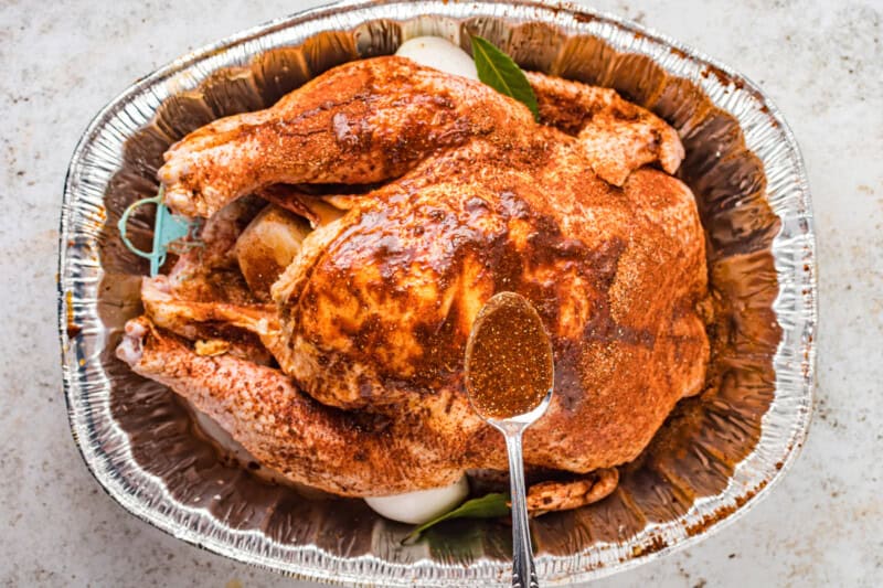 overhead view of juices spooned over a dry brined turkey in an aluminum roasting pan.