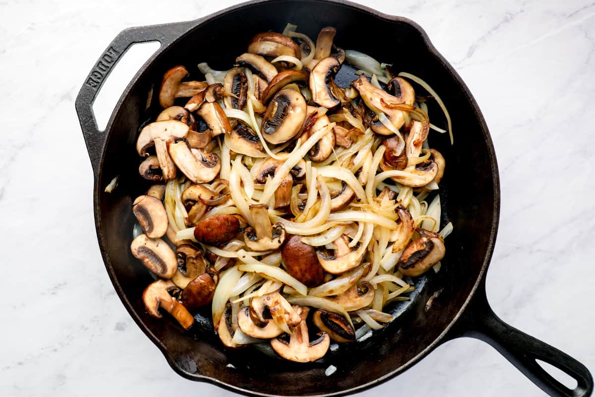 Onions and mushrooms caramelizing in a skillet.