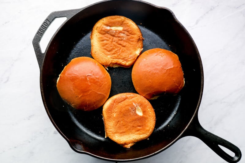 four hamburger buns face down in a skillet