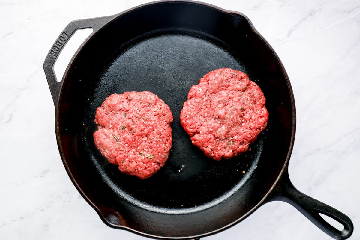 Two uncooked burger patties in a skillet.