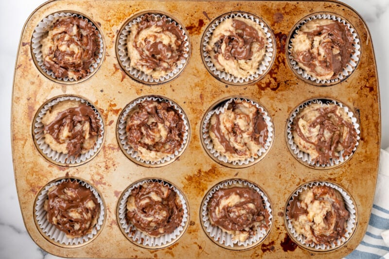 nutella swirled into banana muffin batter in a muffin tin.