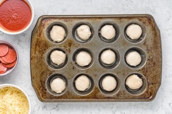 overhead view of dinner roll dough proofing in a cupcake tin.