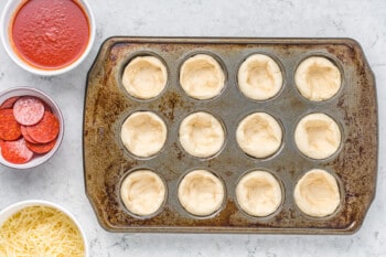 overhead view of dinner roll dough shaped into pizza cups in a cupcake tin.