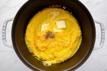 adding grated cheese and pats of butter to a pot of grits