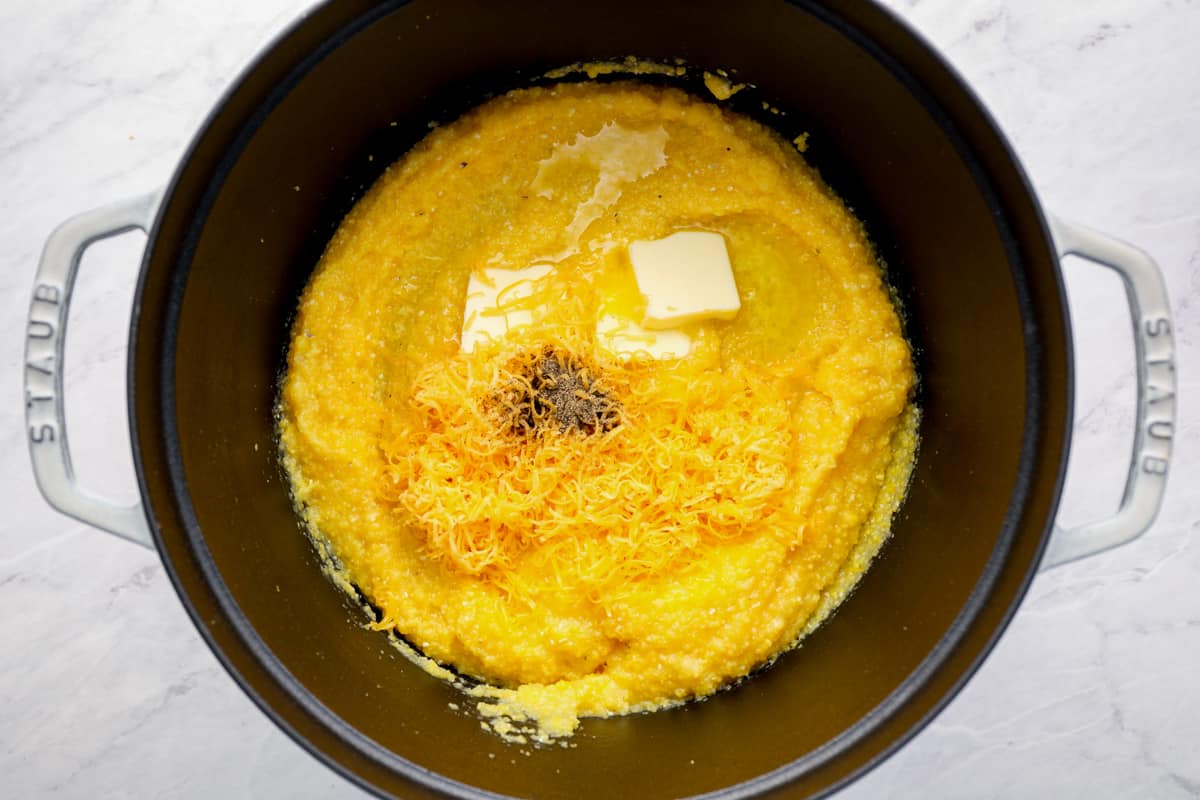 Adding grated cheese and pats of butter to a pot of grits.