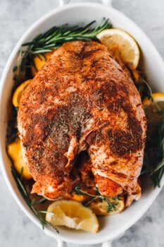 herb rubbed thanksgiving turkey in a white roasting pan with lemons and herbs.