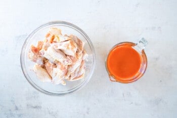 overhead view of chicken wings and buffalo sauce in glass bowls.