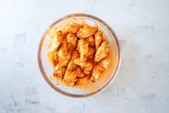 overhead view of chicken wings tossed in buffalo sauce in a glass bowl.