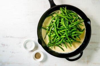 green beans added to cream sauce in a cast iron skillet.