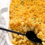 close up of mac and cheese casserole in a white baking pan with a black serving spoon.
