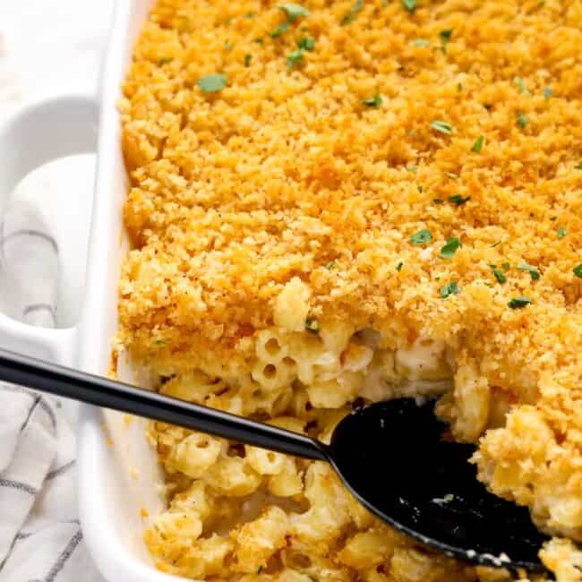 close up of mac and cheese casserole in a white baking pan with a black serving spoon.