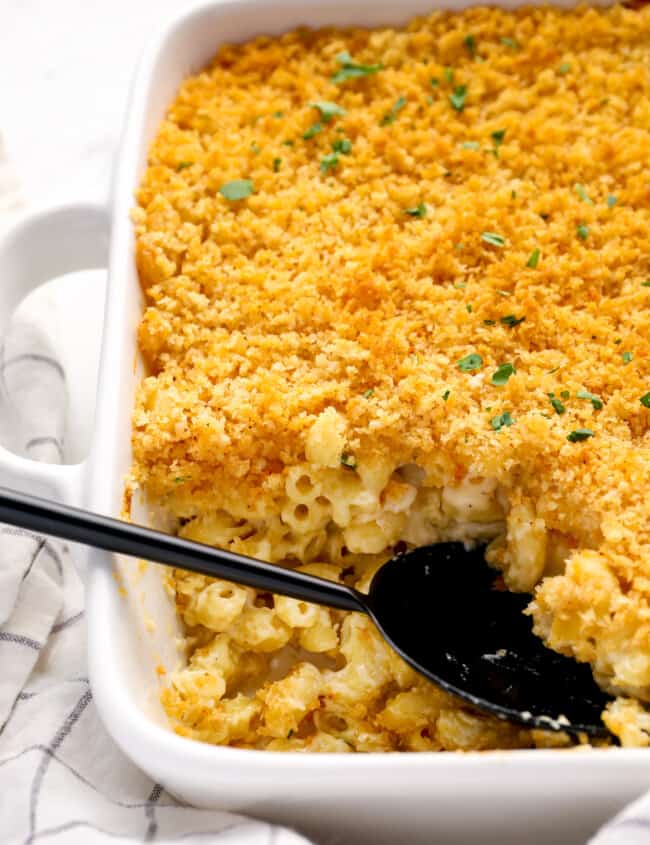 close up of mac and cheese casserole in a white baking pan with a black serving spoon.