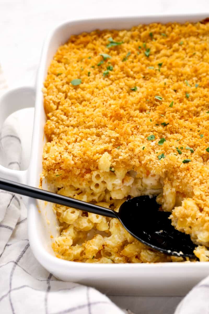 close up of mac and cheese casserole in a white baking pan with a black serving spoon.